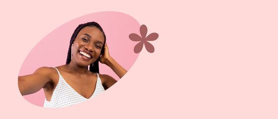 A smiling woman takes a selfie, enjoying a light moment. She wears a casual top while posing against a soft pink backdrop with a simple floral decoration, capturing joy and confidence.