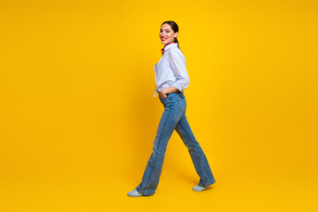 Fototapeta premium Young stylish woman walking confidently in casual fashion against vibrant yellow background, embracing trendy and captivating lifestyle