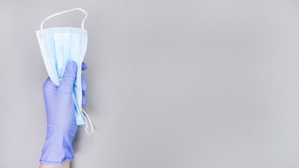 Hand holding multiple disposable face masks with blue latex gloves against a neutral background, emphasizing health and safety during flu season