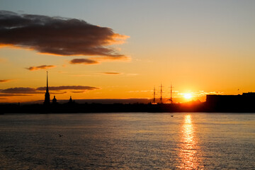 Silhouettes of city buildings against the backdrop of the setting sun, reflected in the waters of the river
