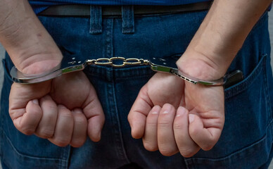 Arrested person in jeans with hands in cuffs