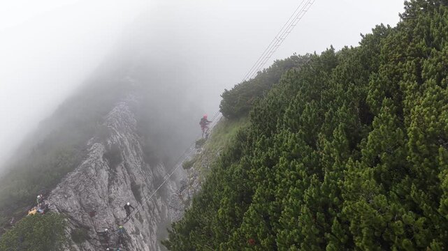 Adventurous hiker cautiously crossing a suspension bridge in foggy mountains, Dachstein, Austria