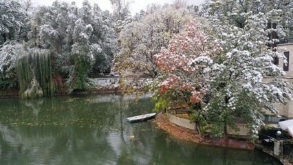 Fototapeta premium First snow falling on autumn trees lining river