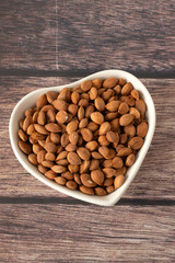 Raw almond seeds in a heart shaped dish on wooden table. Top view.