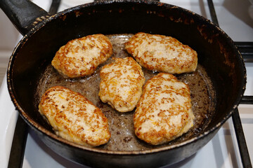 Meat cutlets are fried in black pan. Five cutlets are cooking, frying meat