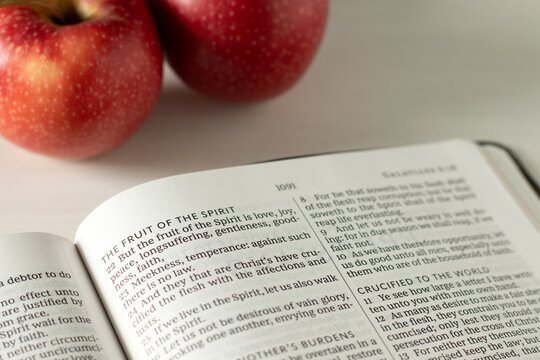 Fruit of the spirit inspirational biblical text in open holy bible book with apples. Christian spiritual growth, love, joy, peace, and obedience to God Jesus Christ concept.