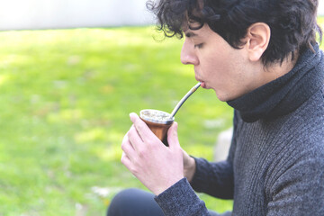 Guy with curly hair sitting in the park enjoying a warm mate