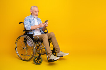 Grandpa in wheelchair using smartphone against bright yellow background showcasing accessibility...