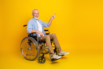 A cheerful grandpa in a wheelchair points to the right against a bright yellow background in a...