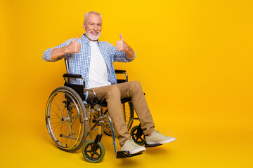 grandpa in wheelchair smiles and shows thumbs up wearing blue checkered shirt in bright yellow...