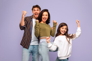 Obraz premium Victory concept. Overjoyed family of three shaking clenched fists, making winner gesture, posing over purple studio background