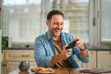 Happy man enjoying mobile gaming on phone at home