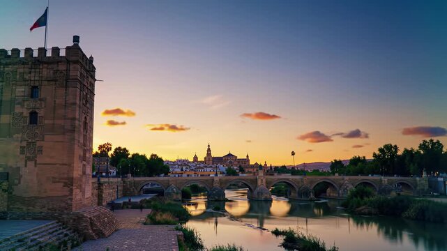 Wide establishing video of C&oacute;rdoba, Spain's Calahorra Tower & Roman Bridge over Guadalquivir, leading to Mezquita-Cathedral at dramatic sunset, anamorphic, deep focus. Timeless awe-inspiring ambiance
