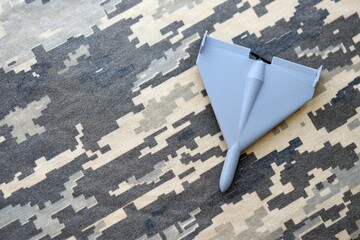 Unnamed grey toy drone model on camouflage fabric close up. Kamikaze drone for bombing targets