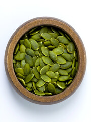 Top view of green pumpkin seeds in a wooden bowl on a white background