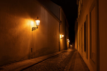 Hradcany, Prague, Czech Republic, Czechia. Empty narrow street in old town. Historical city at night. Lanterns and yellow artificial light.