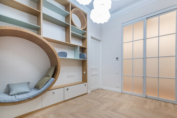 Bright room showcases a unique circular seating area with soft cushions, minimalist wall shelves, and a stylish sliding door. The warm wood floor adds to the modern aesthetic.