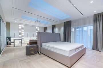 This spacious bedroom showcases a minimalist design with natural light flowing through large windows. An unmade bed takes center stage, complemented by stylish furniture and decor.