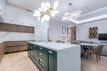 Bright and spacious kitchen with a large island and modern cabinetry. The sleek design includes a dining area and unique lighting fixtures, creating a warm atmosphere in the apartment.
