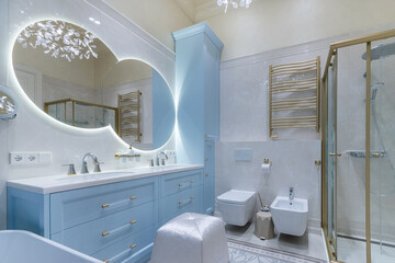 Soft blue cabinetry and gold accents create a serene atmosphere in this modern bathroom. A large mirror and glass shower enhance the space’s bright feel, perfect for relaxation.