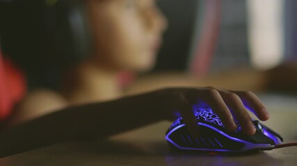 Close-up of a gaming mouse illuminated by RGB light, with a boy wearing a headset blurred in the background, his face softly glowing from the computer screen at night. - Powered by Adobe