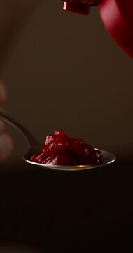 Vertical macro video of ketchup pouring into a spoon on dark background. Appetizing closeup food concept 4k