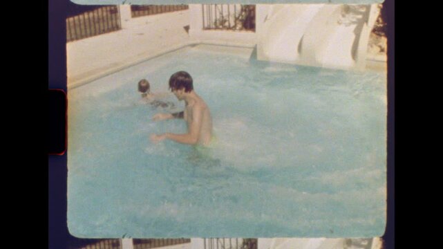 Fourteen year old boy and his eight year old sister sliding into a backyard pool on a sunny day with retro summer vibes