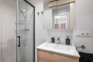 Modern bathroom with a glass shower, white tiles, and a wooden vanity. The space is well-lit and features a mirror above the sink.