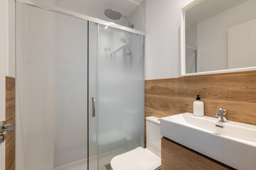 Modern bathroom with a glass shower, wooden accents, and a sleek sink. Bright and clean design with minimalistic decor.