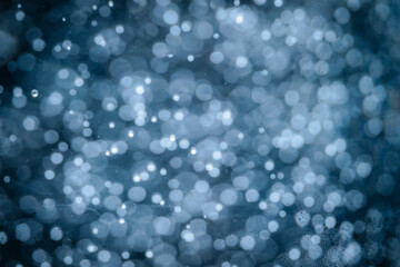 Abstract blue bokeh lights creating a dreamy, sparkling effect that resembles soft snow or underwater bubbles.