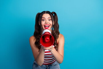 Fototapeta premium Energetic young woman holding a red megaphone in a vibrant pose against a blue background, expressing excitement and enthusiasm