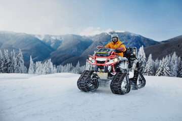 Snowy mountain adventure with a quad bike in winter, showcasing excitement in a picturesque landscape of mountains and trees under a clear blue sky © verona_studio