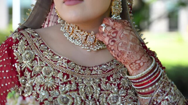 Red and gold colors in the traditional wedding Indian clothes, Close up view of embroidered dress and bride henna painted hands touching the necklace