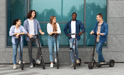 Urban Lifestyle. Group of five multiracial friends talking and standing on motorized kick scooters in the city © Prostock-studio