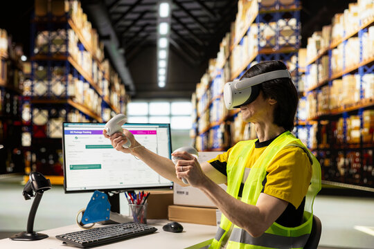 Asian man uses virtual reality headset and tracking software near industrial storage racks, processing e-commerce orders. VR device to update tracking info on parcels, artificial intelligence.