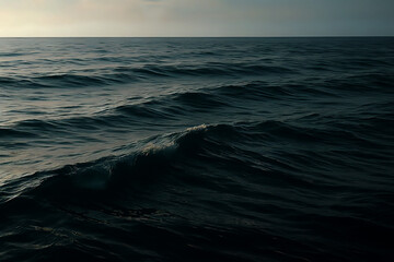 Dark ocean waves under soft evening light, capturing the natural movement and tranquil depth of the sea surface. Gentle highlights reveal rich tones of blue, teal, and muted silver reflections.