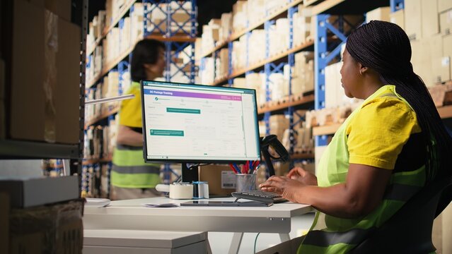 Warehouse employee using package tracking software on computer monitor, managing express delivery and using awb tracking info to update real time parcel status. Distribution hub. Camera A.