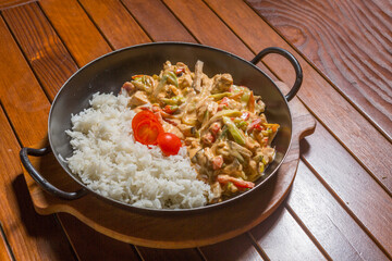 Delicious creamy chicken and vegetable stir fry served with white rice and cherry tomatoes on a wooden table