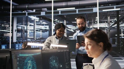Data scientists working together in server room, reviewing neural network code and LLM visualization dashboards. Team of IT experts coordinating tasks, monitoring AI system performance, camera A