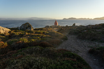 Punta Robaleira red lighthouse in Home cape at sunset in Rias Baixas zone in Galicia coast with Cíes islands in the background.