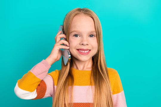 Smiling young girl talking on smartphone against teal background showing cheerful mood and modern communication