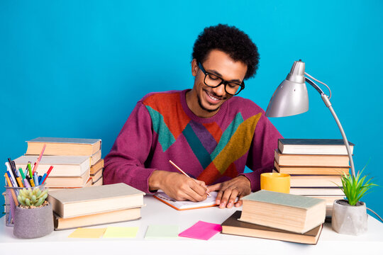 Young man confidently studying at desk surrounded by books and stationery in vibrant minimalistic modern bright space