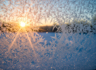Snowflakes on windshield. Frosty window with ice crystals and sunrise in winter landscape  