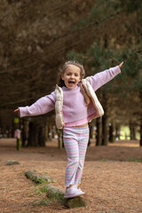Fototapeta premium Joyful child balancing on a log in autumn forest adventure. Childhood