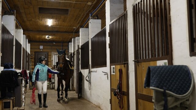 Female equestrian rider walking with her horse inside a stable - Powered by Adobe