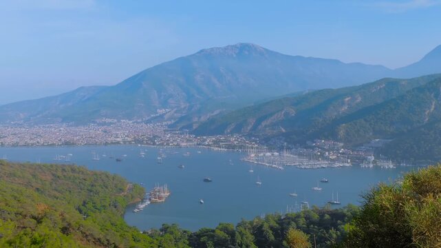 Time lapse: anchored yachts and gulets in Fethiye bay, some boats are gliding fast across the water against lush mountain and green hillsides backdrop. Marine tourism, timelapse and travel concept