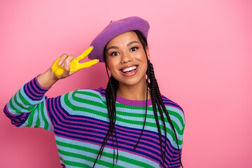 Naklejka premium Smiling young woman in stylish striped sweater making peace sign gesture against pink background, joyful and trendy
