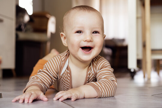 Happy, laughing baby lying on tiled floor at home for child development, wellness and growth. Cheerful active little infant kid training physical skills, smiling, learning to crawl, playing and relax.