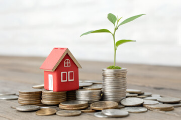 A conceptual image showing a small red house model placed on stacked coins with a green sprouting plant on top ,symbolizing financial growth,savings, home investment  and sustainability 