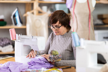 Working in sewing workshop - female dressmaker working at a sewing machine making stitches on fabric